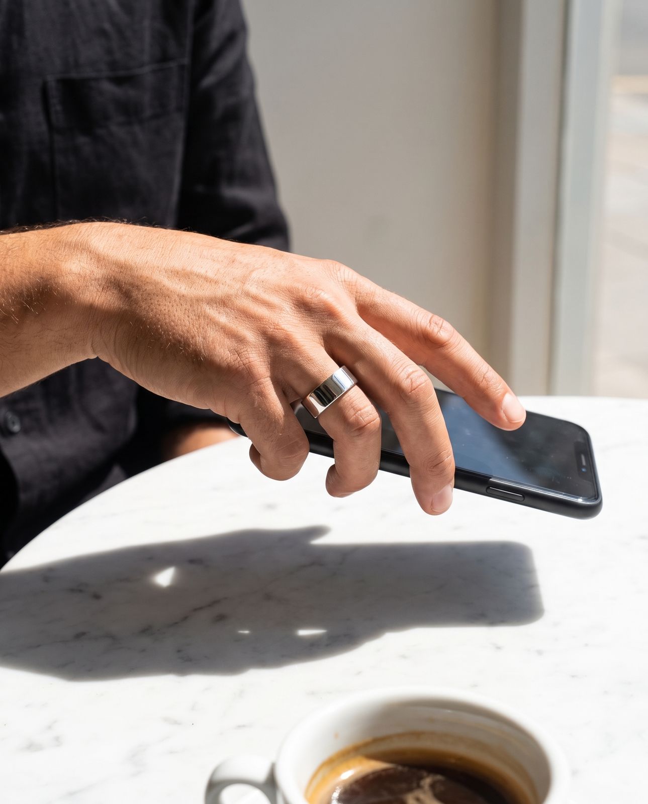 A ringed hand placing a phone face-down on a sunlit table