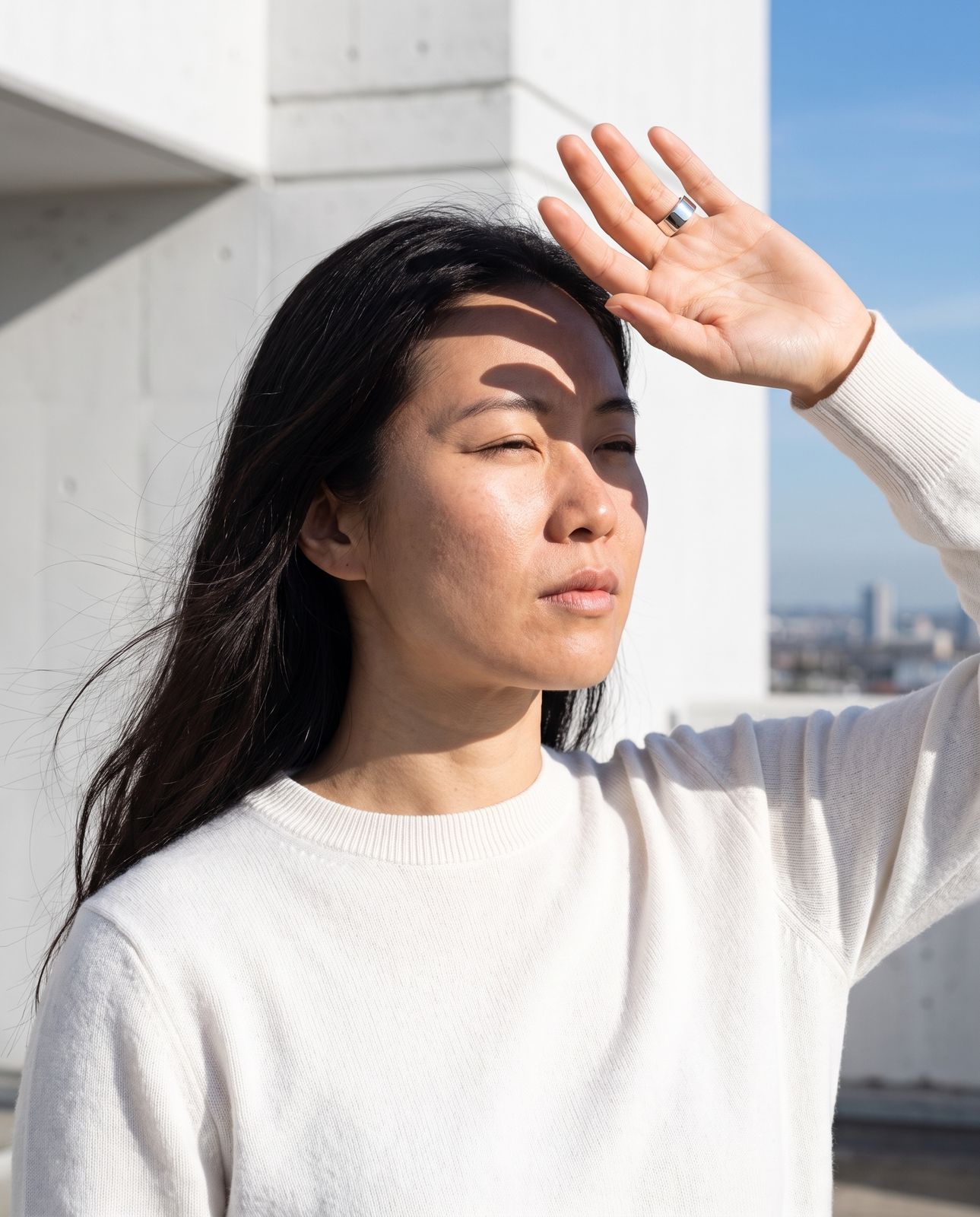 A woman shielding her eyes from the sun with her ringed hand, smiling into the light